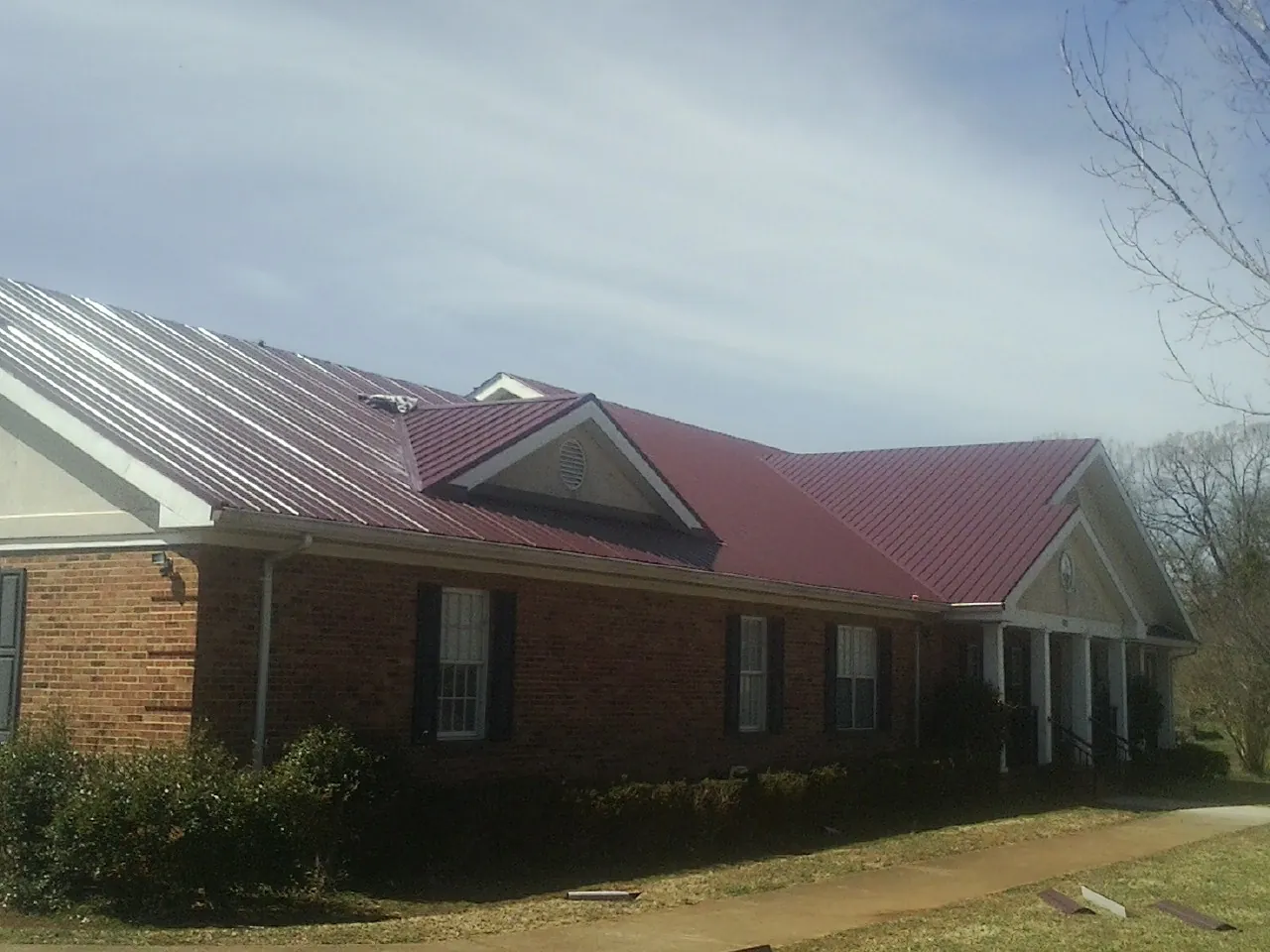 Red metal roof with gabled entries on a long brick building, from a Hail Damage Roof Repair job in South Fallsburg