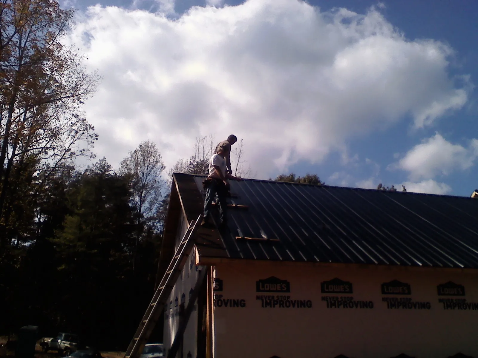 Roofer fastening dark metal panels high against a cloudy sky, from a Roof Inspection job in South Fallsburg