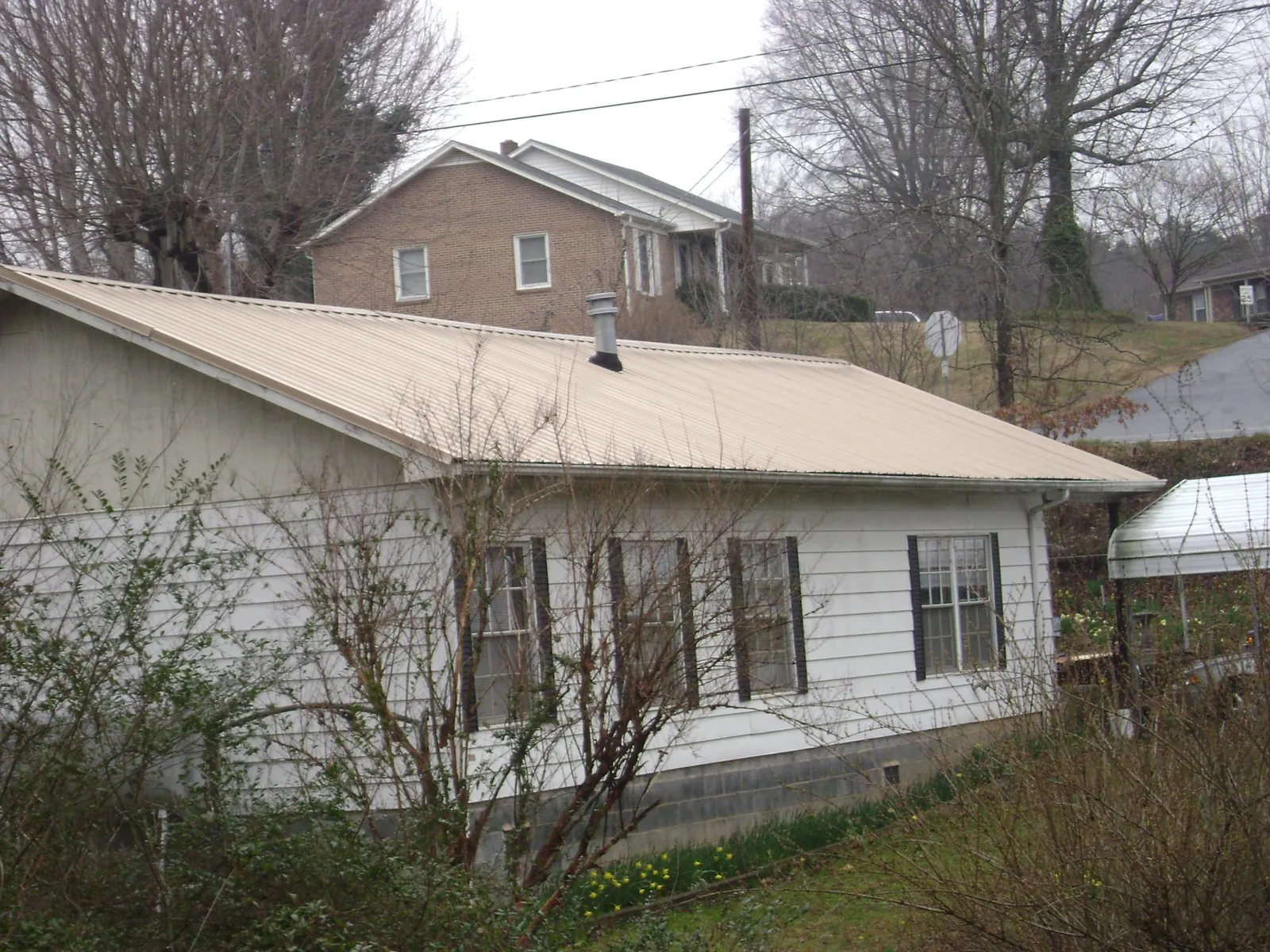 Tan metal roof on a white sided house set into a hillside — Commercial Roofing by Roofing Brothers in South Fallsburg